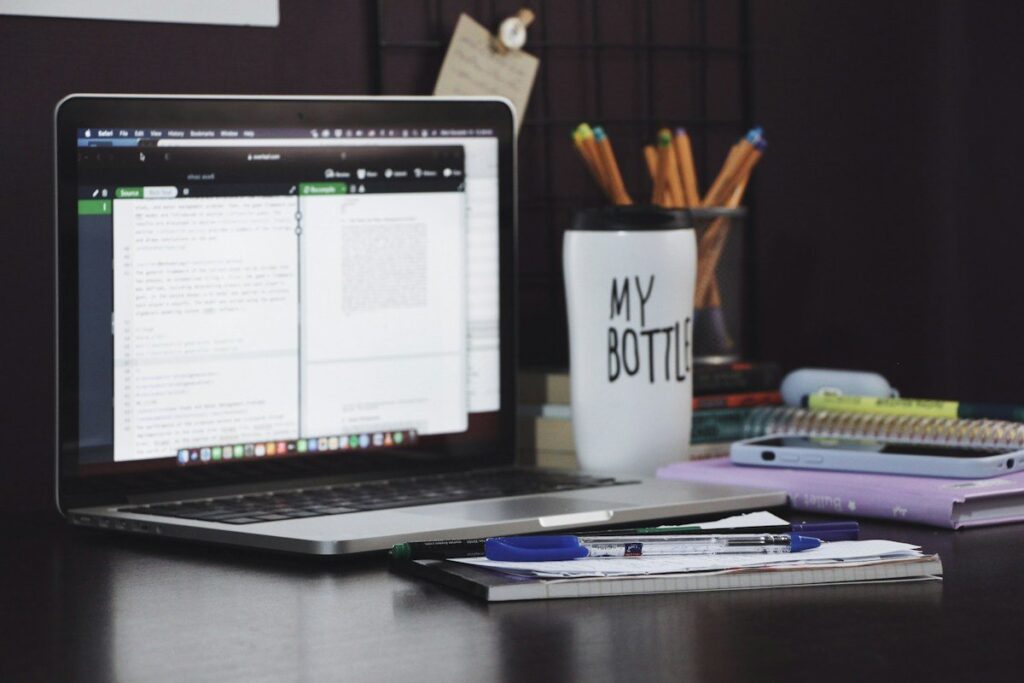 Laptop with a document open beside a notebook and pencil pot