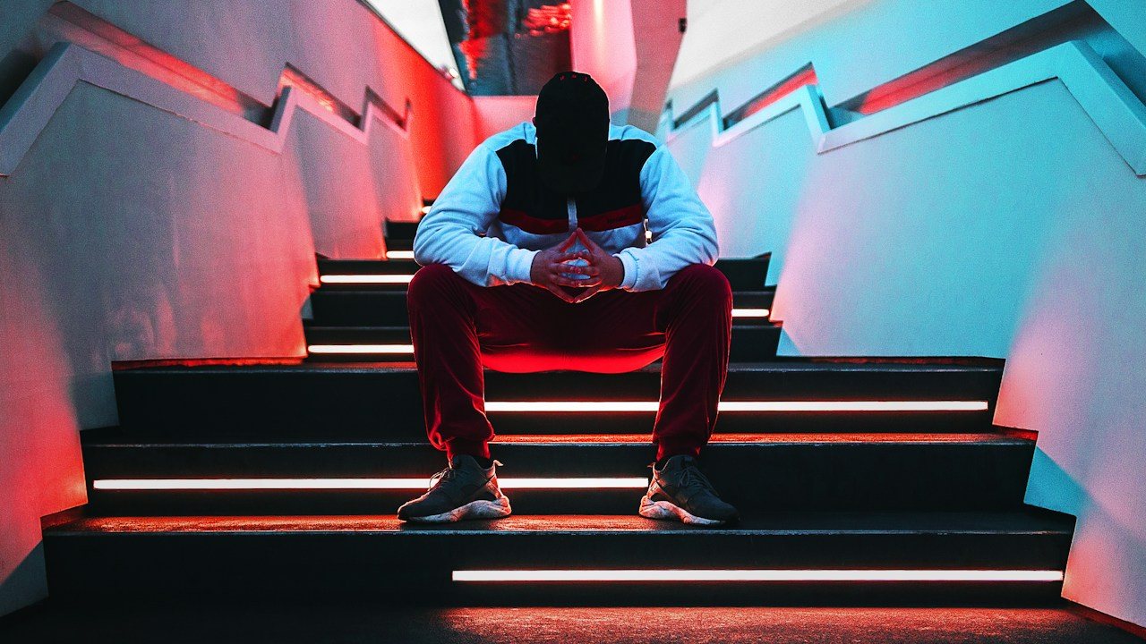 Man sitting on stairs with his head in his hands after a loss, the moment revenge trading starts