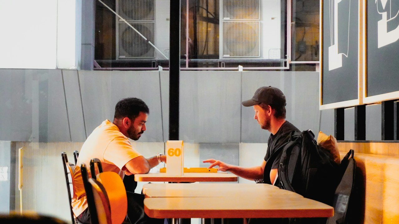 Two men talking across a cafe table, comparing supply and demand with support and resistance