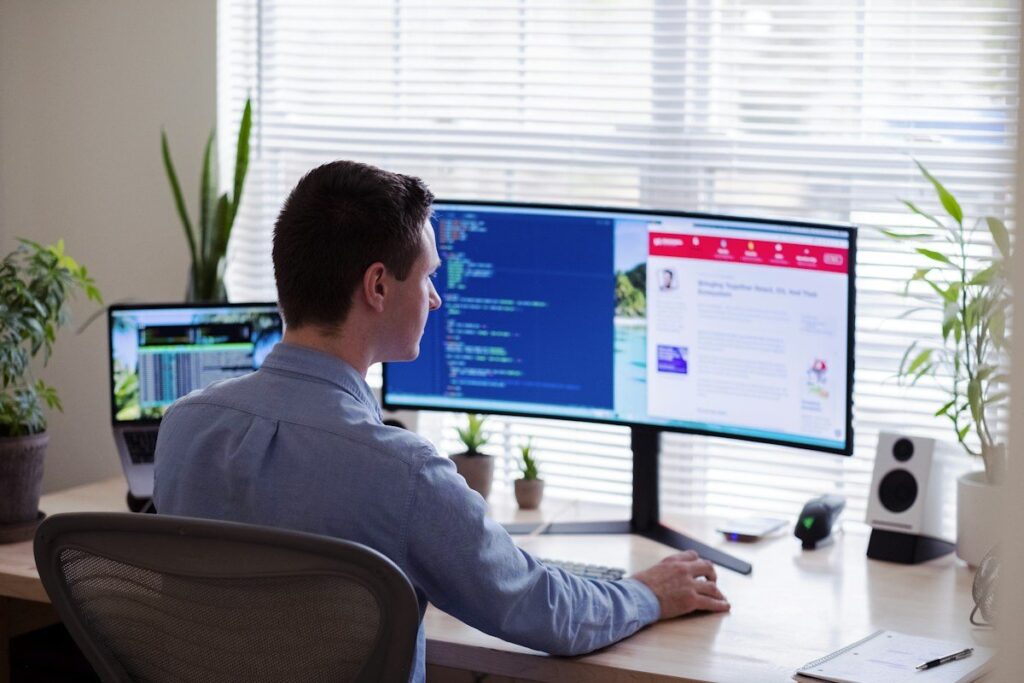 Man at a desk in front of a curved monitor by a window