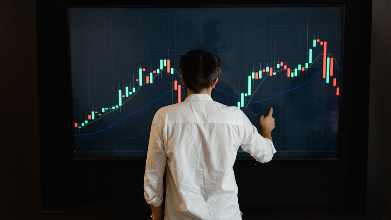 Trader in a dark room looking at a large monitor with a rising candlestick chart