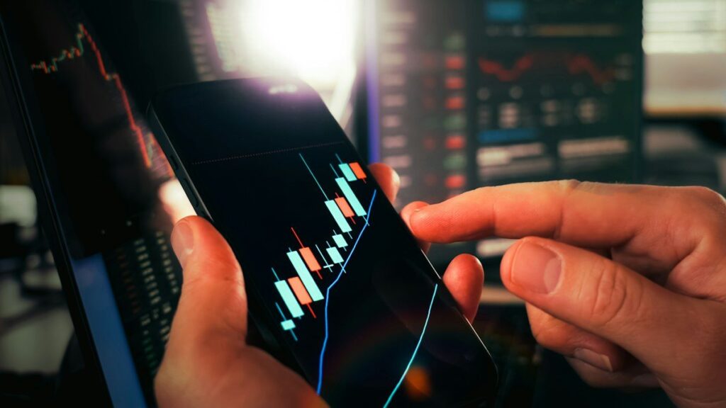 Hands holding a phone with a candlestick chart
