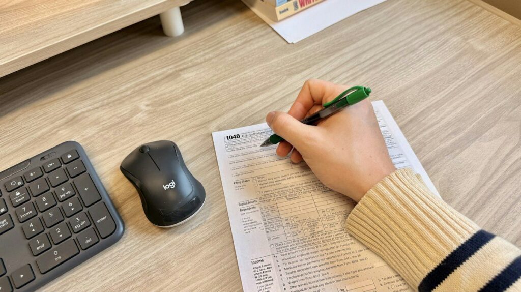 Person writing on a printed sheet beside a keyboard and mouse