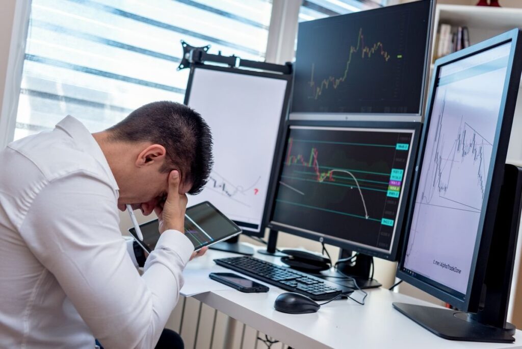 Man with his head in his hands at a desk of chart monitors
