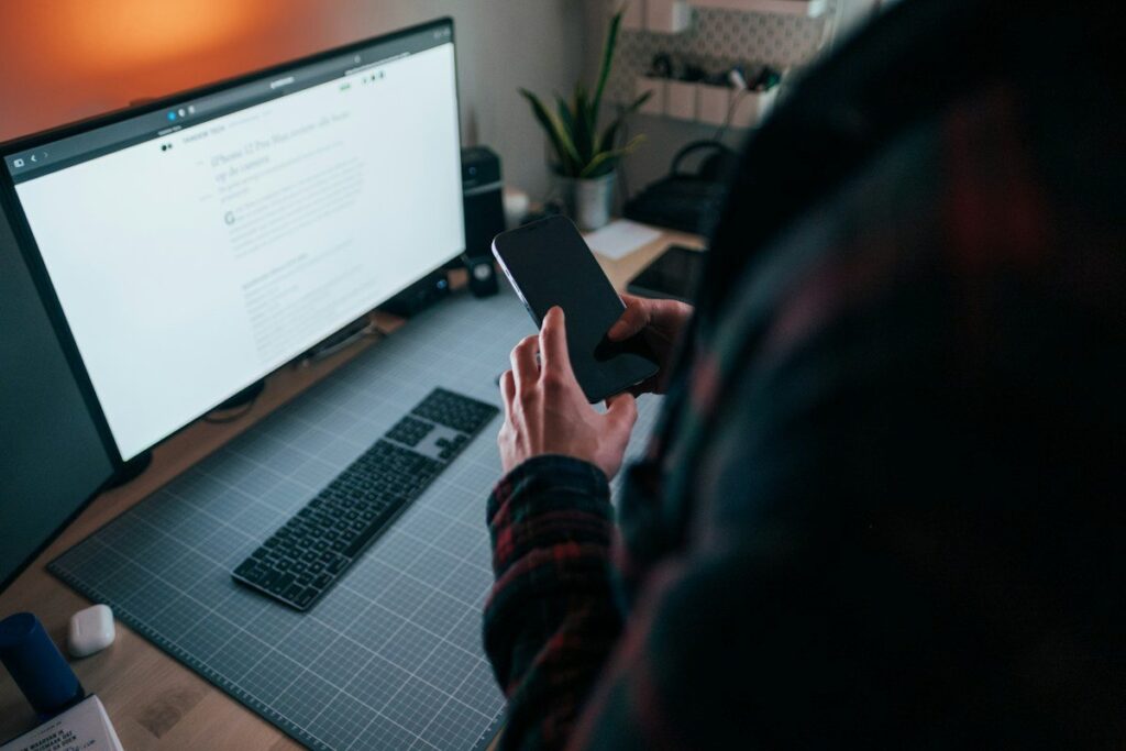 Person checking a phone beside a monitor, using an indicator to confirm a price action idea