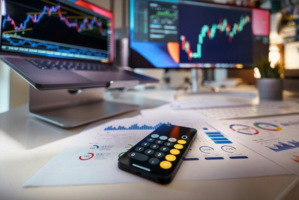 Calculator in front of monitors showing stock charts