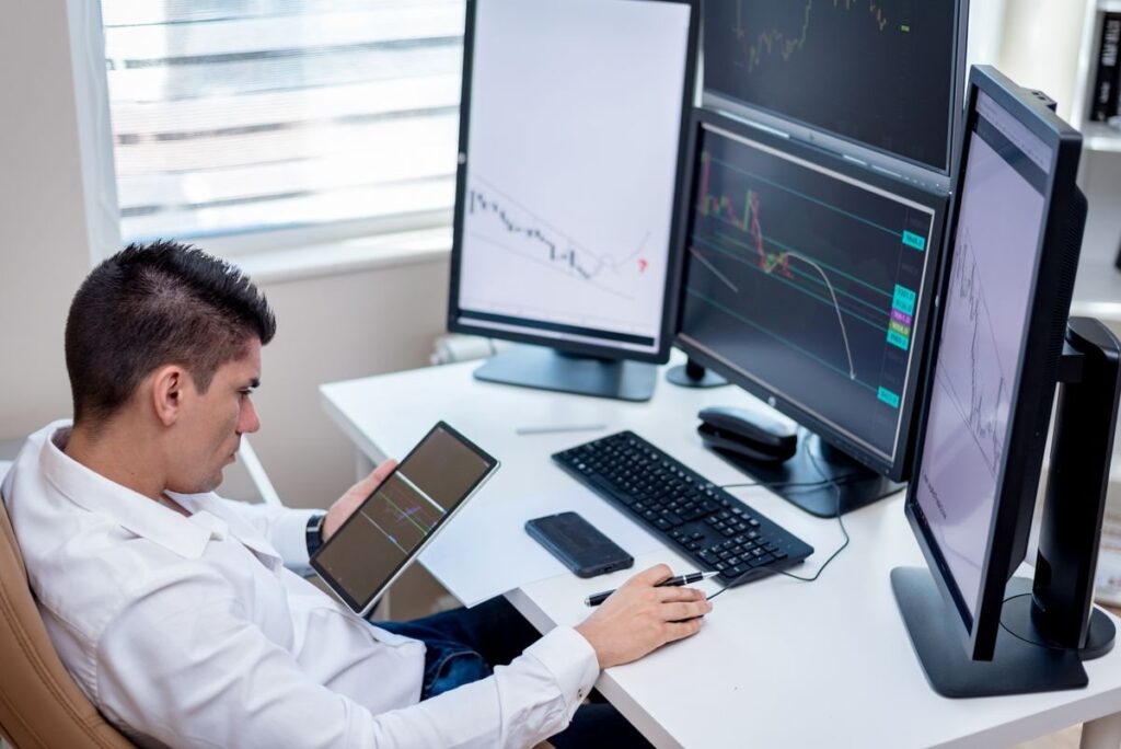 Trader at a desk with several monitors, holding a tablet