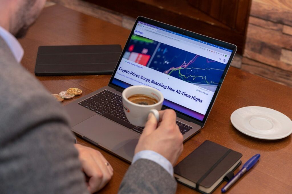 Man with a coffee cup at a laptop showing a market news page
