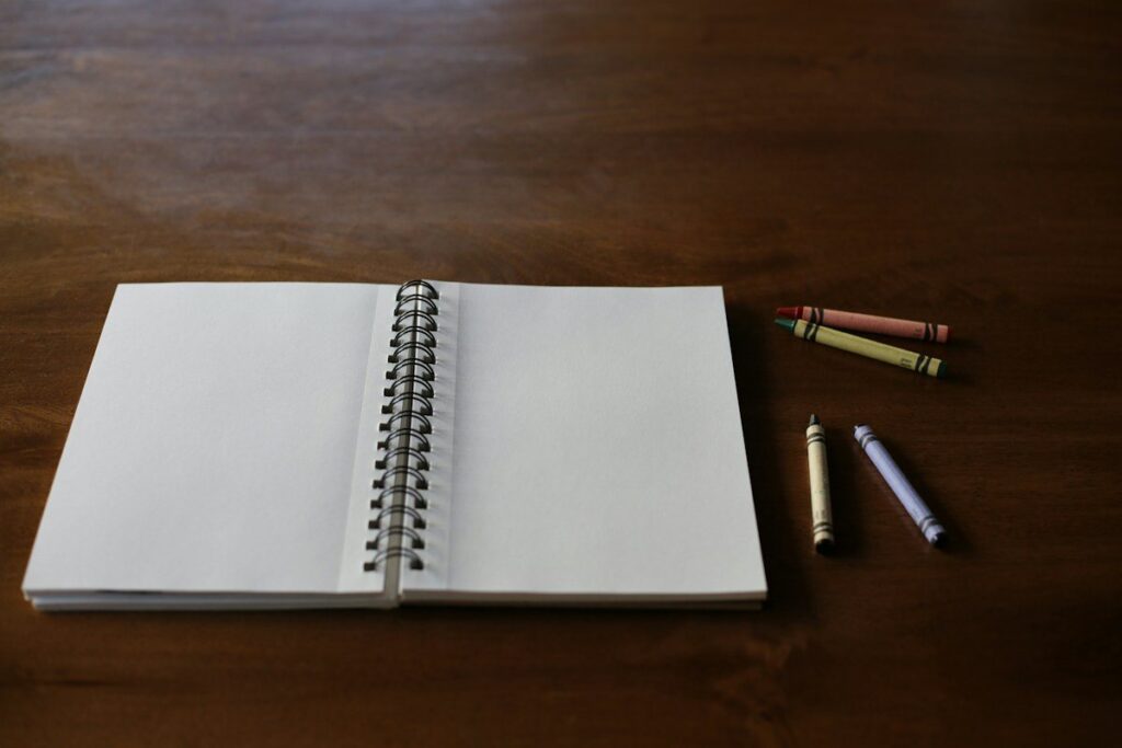 Open spiral notebook and crayons on a desk, ready for separating a trading strategy, system and plan