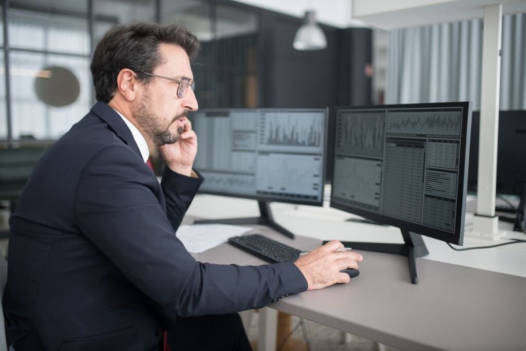 Man on a phone at a desk with two monitors