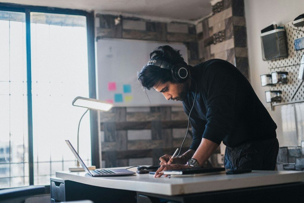 Man in headphones writing at a standing desk in a home office