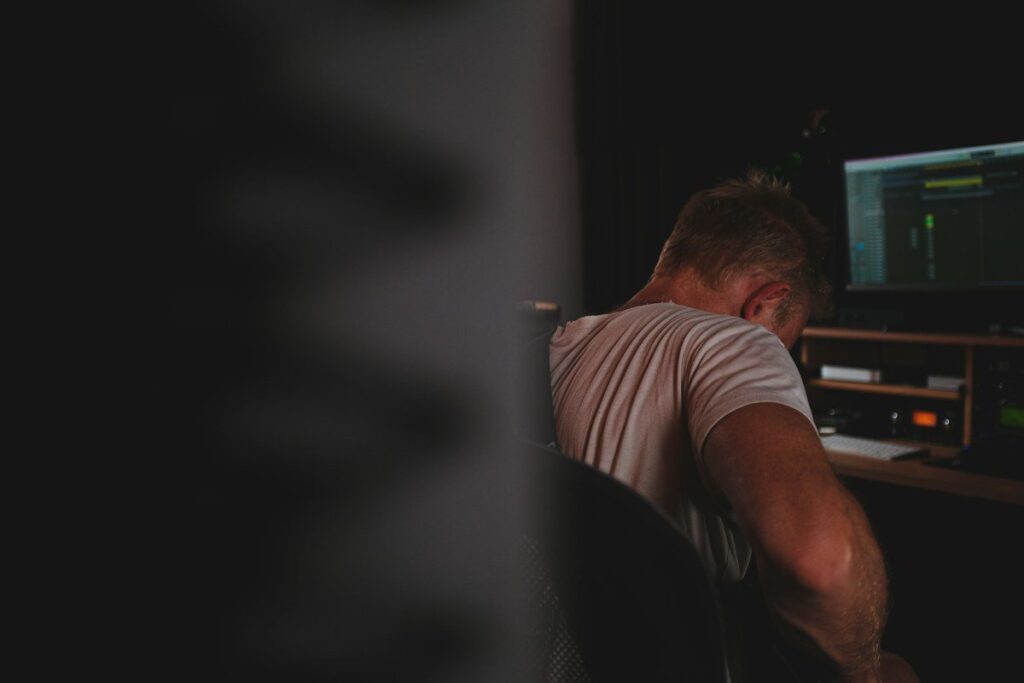 Man with his head down at a desk in a dark room