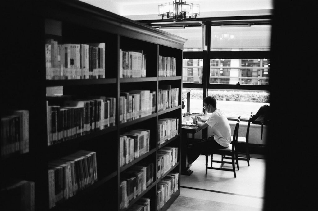 Person focused on one laptop in a quiet library, the habit of learning one forex pair at a time