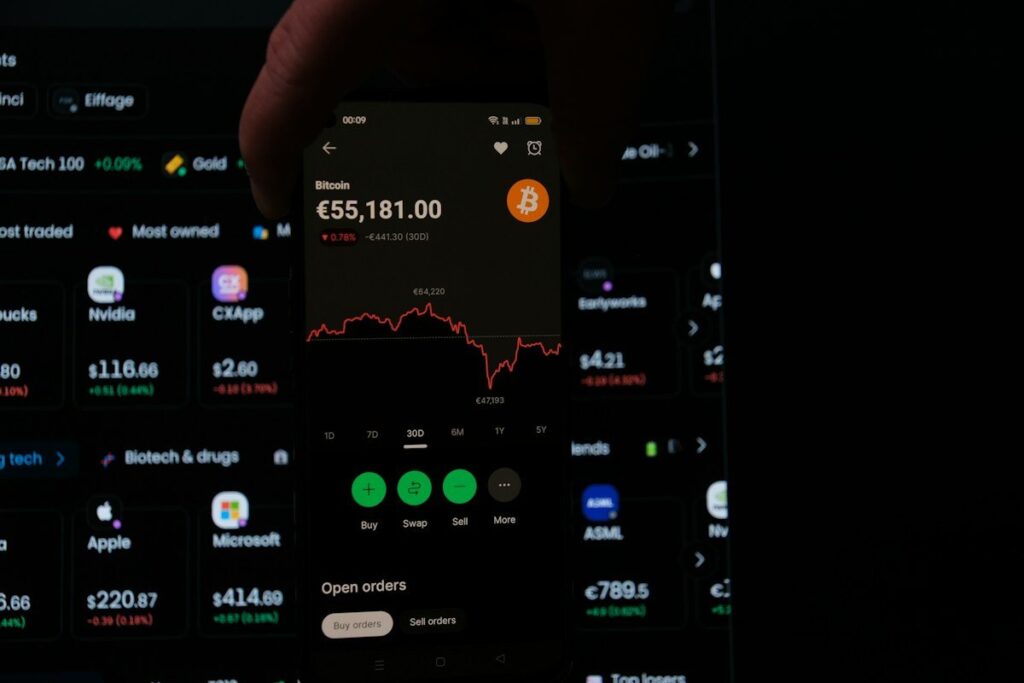 Hand holding a phone with a trading app in front of a screen
