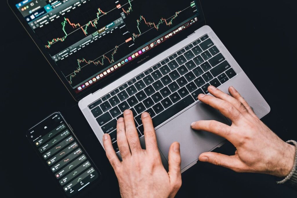 Hands typing on a laptop beside a tablet showing charts