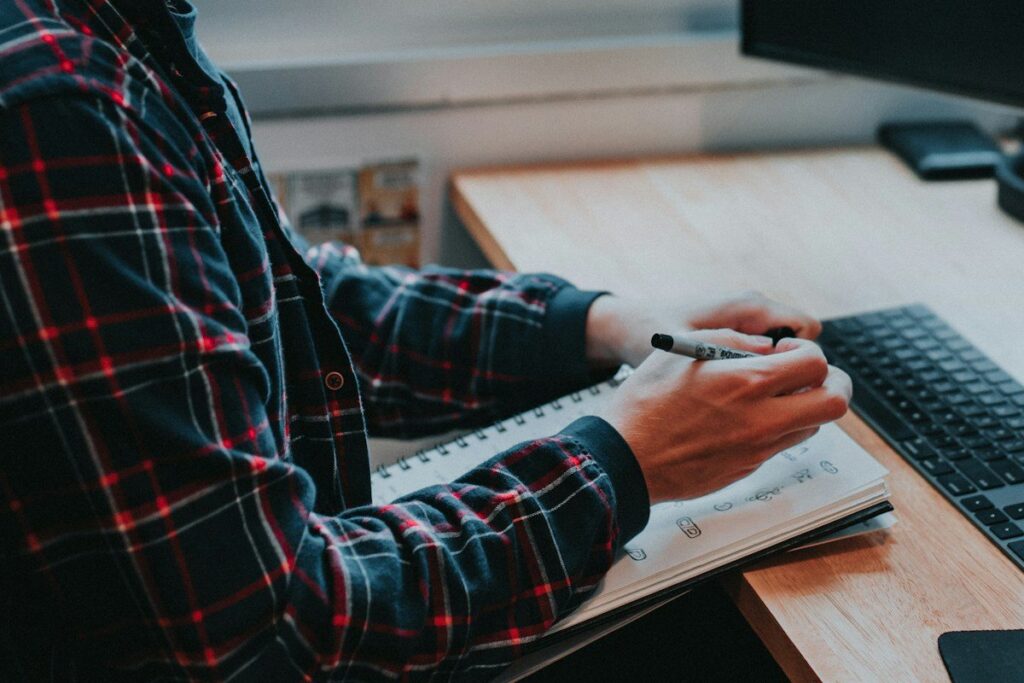 Hand writing in a notebook beside a keyboard
