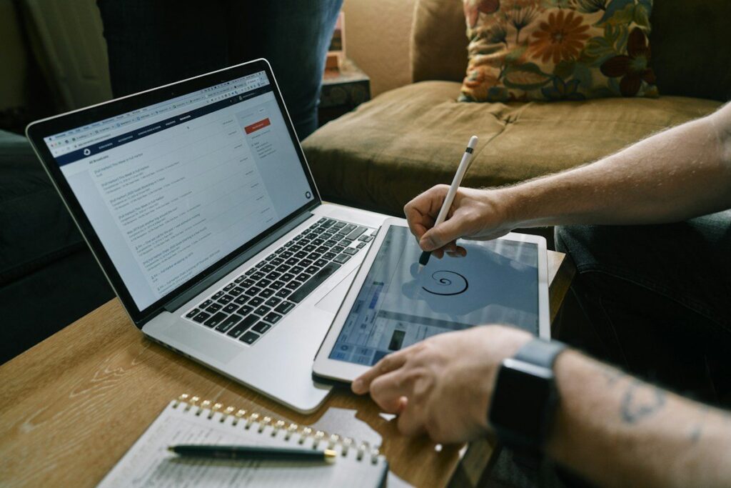 Person writing on a tablet with a stylus beside a laptop and a notebook
