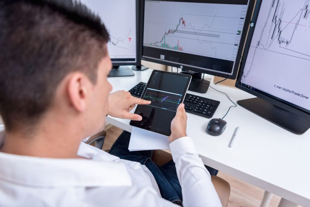 Man holding a tablet at a desk with several chart monitors