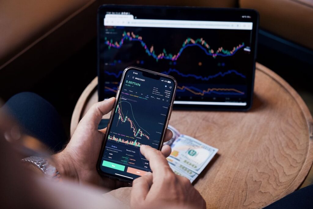 Hands holding a phone showing a candlestick chart in front of a tablet chart