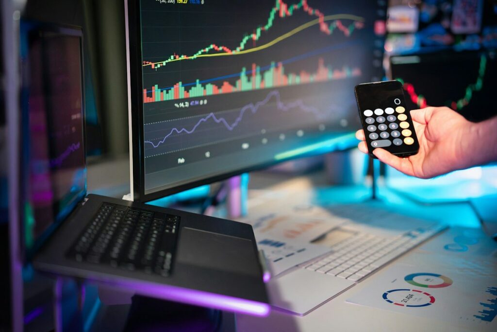 Hand holding a phone calculator in front of chart monitors