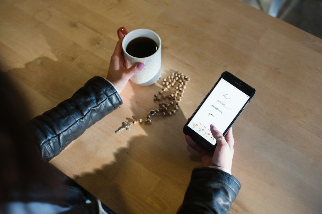 Person holding a phone and a cup of coffee at a wooden table