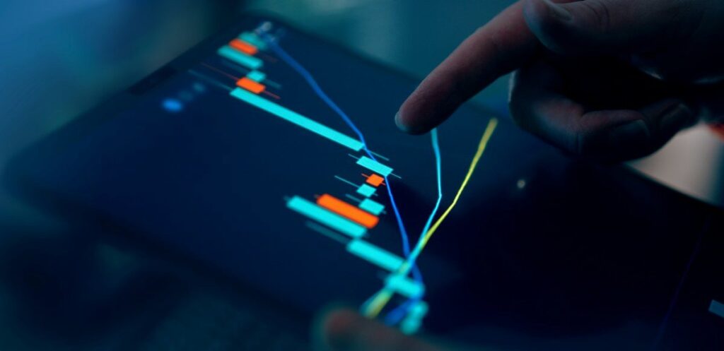 Finger touching a screen showing a candlestick chart