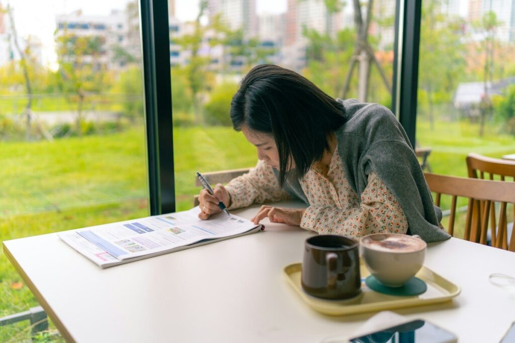 Person writing on a printed sheet at a table by a window, reviewing trading rules before the session