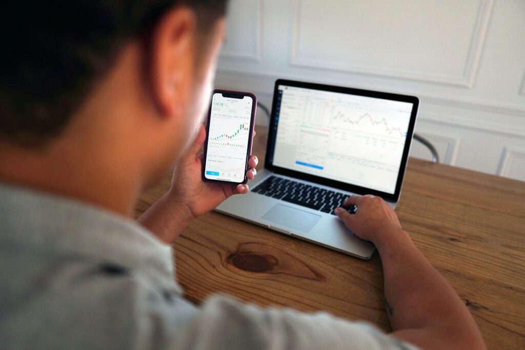 Person holding a phone in front of a laptop showing charts