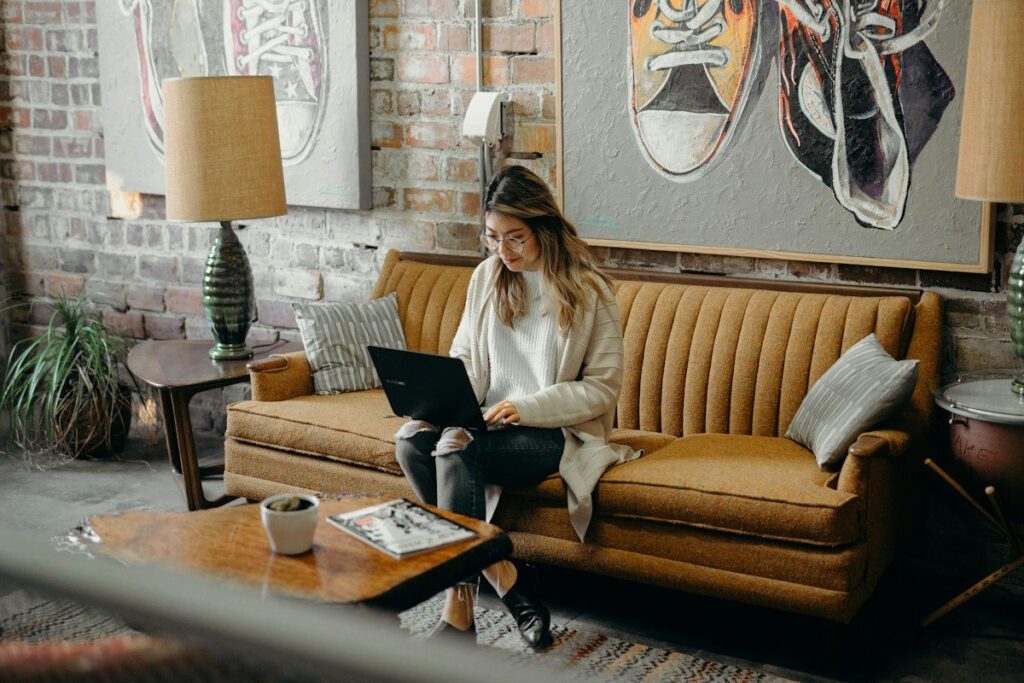 Woman using a laptop on a sofa at home, checking where she took profit on past trades