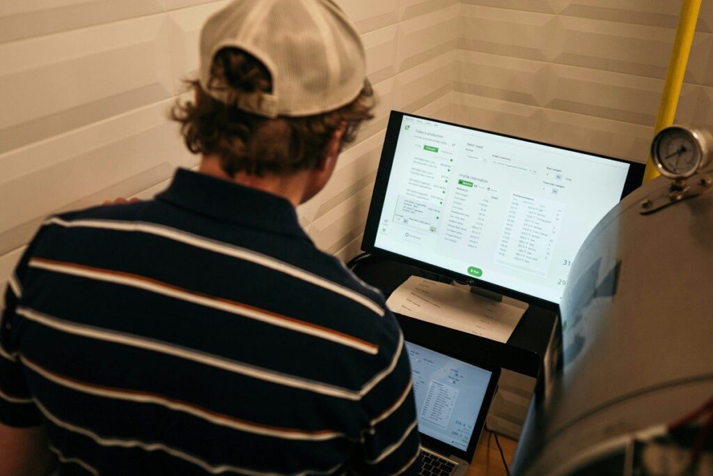 Man in a cap looking at a monitor showing a table of figures