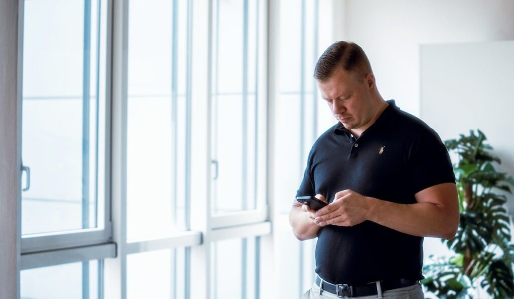 Man checking his phone by an office window