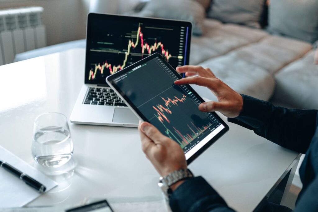 Hands holding a tablet with a chart beside a laptop