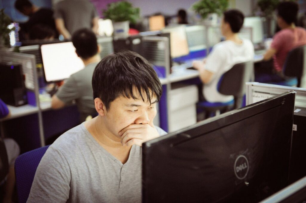 Man with his hand over his mouth at a monitor in an office