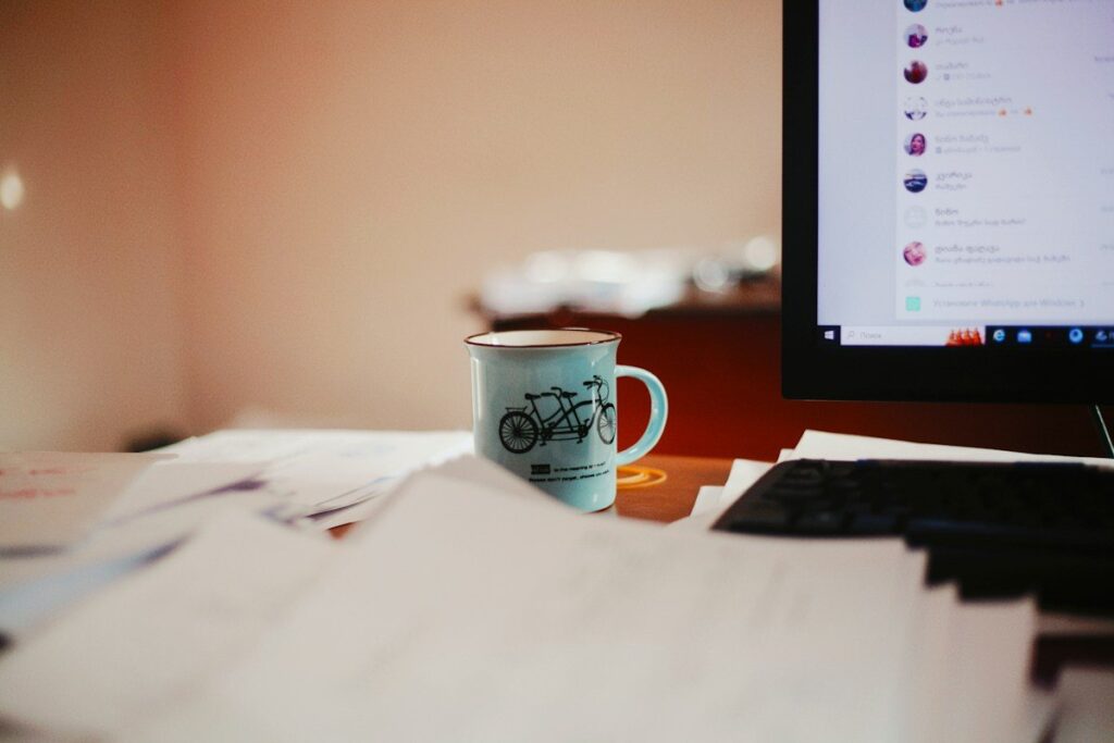 Printed papers and a mug beside a monitor on a desk