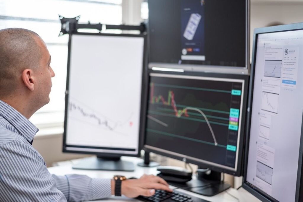 Man in a striped shirt watching a falling chart on one of several monitors