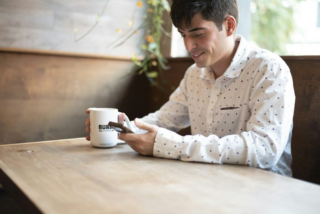 Man smiling at his phone at a cafe table