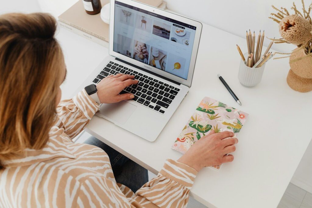 Woman typing on a laptop at a white desk beside a notebook