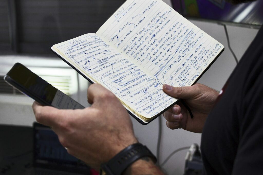 Hands holding a phone and an open notebook of handwritten notes