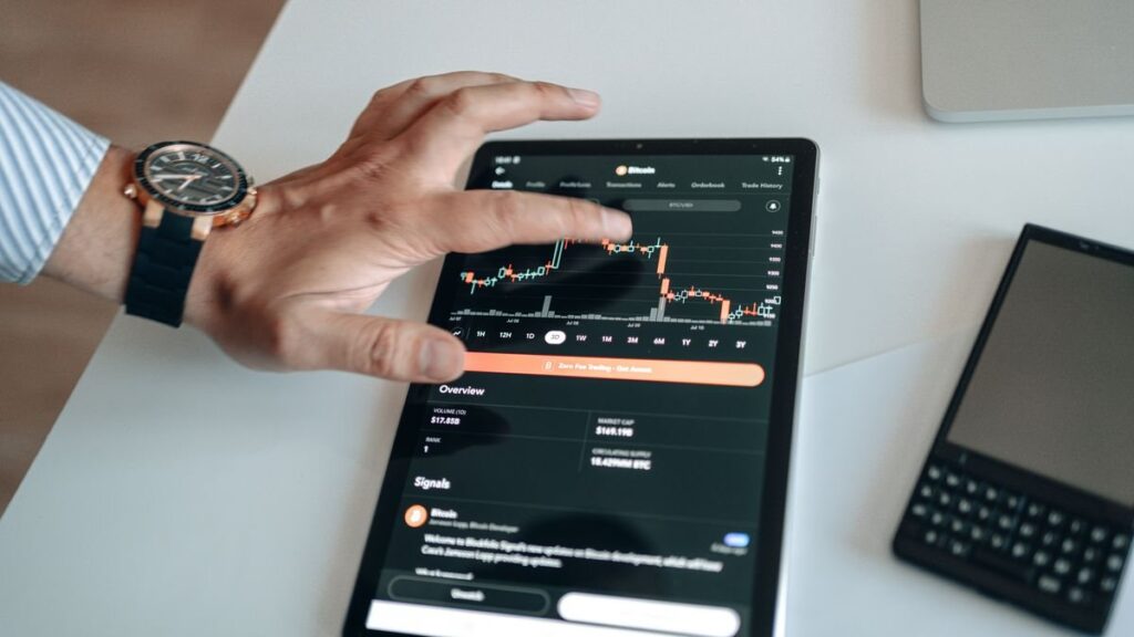 Hand on a tablet showing a trading app chart