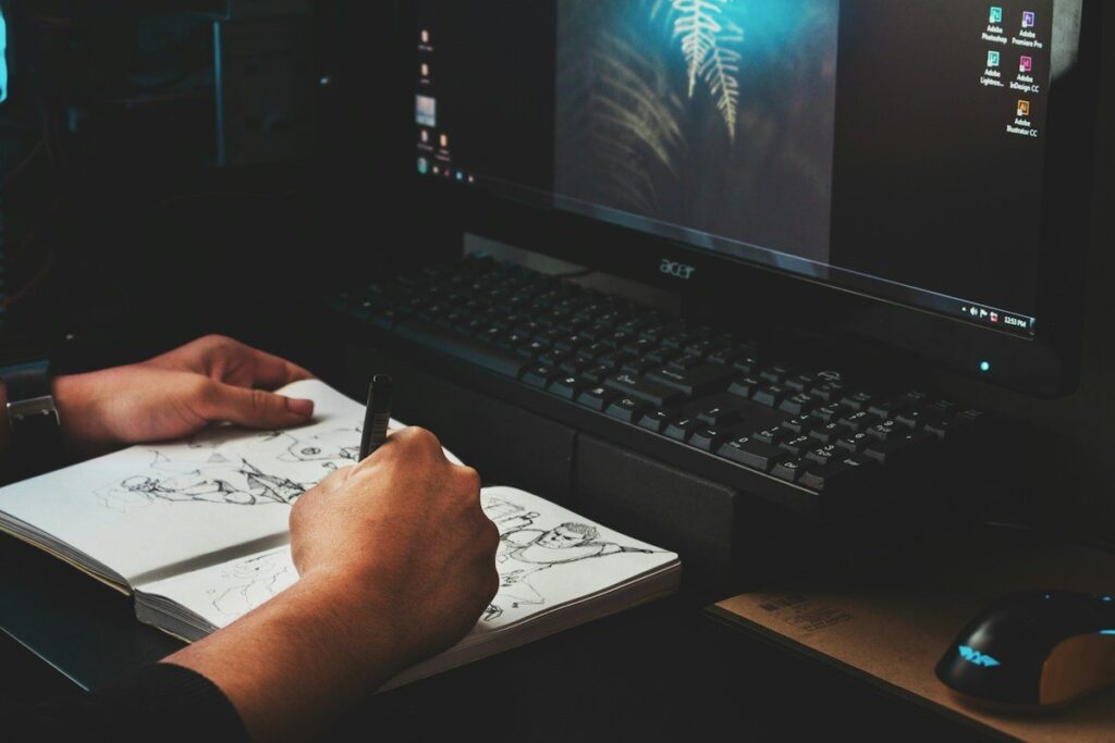 Hand sketching in a notebook beside a keyboard