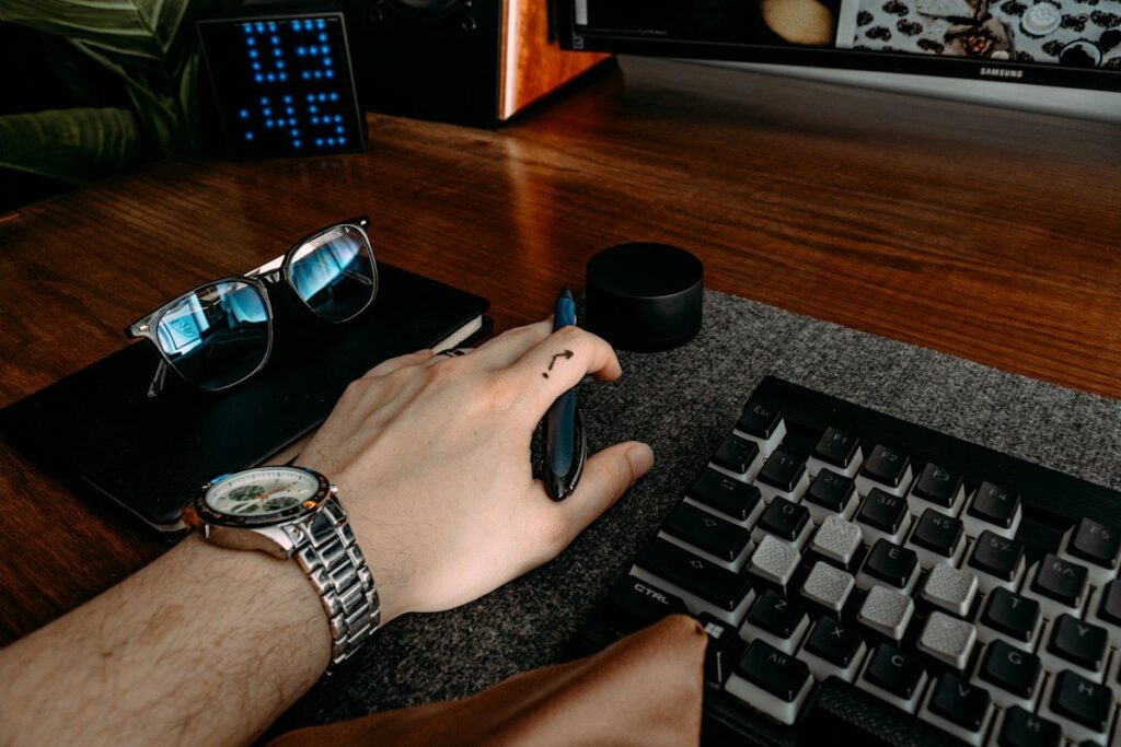 Hand on a keyboard beside a pair of glasses
