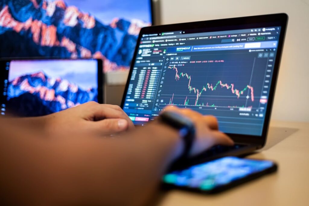 Hands on a laptop showing a candlestick chart, with a phone alongside