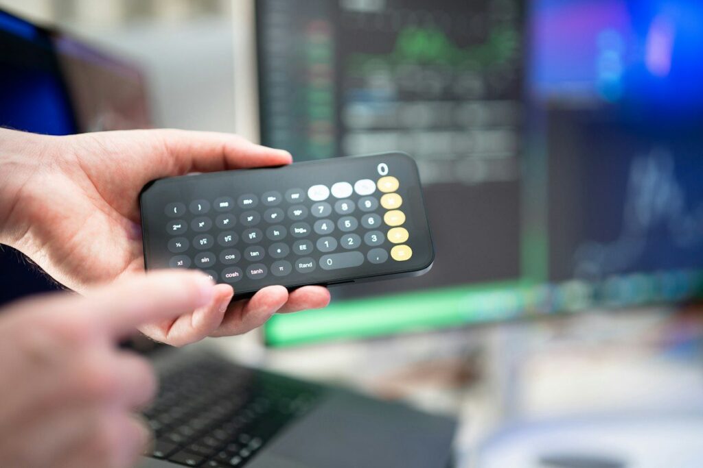 Hand holding a calculator in front of trading screens
