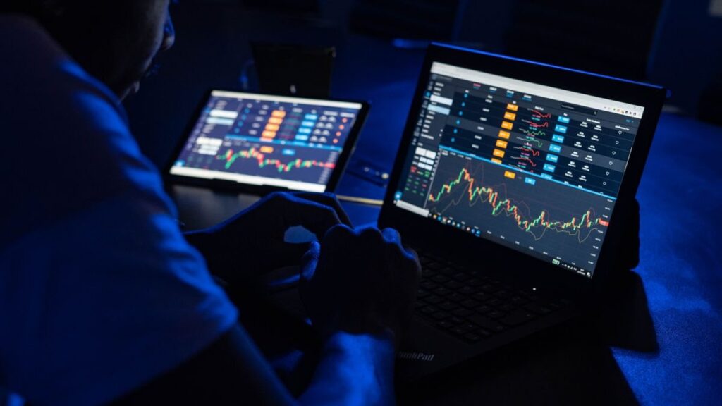Trader studying candlestick charts across two monitors while watching a price range narrow