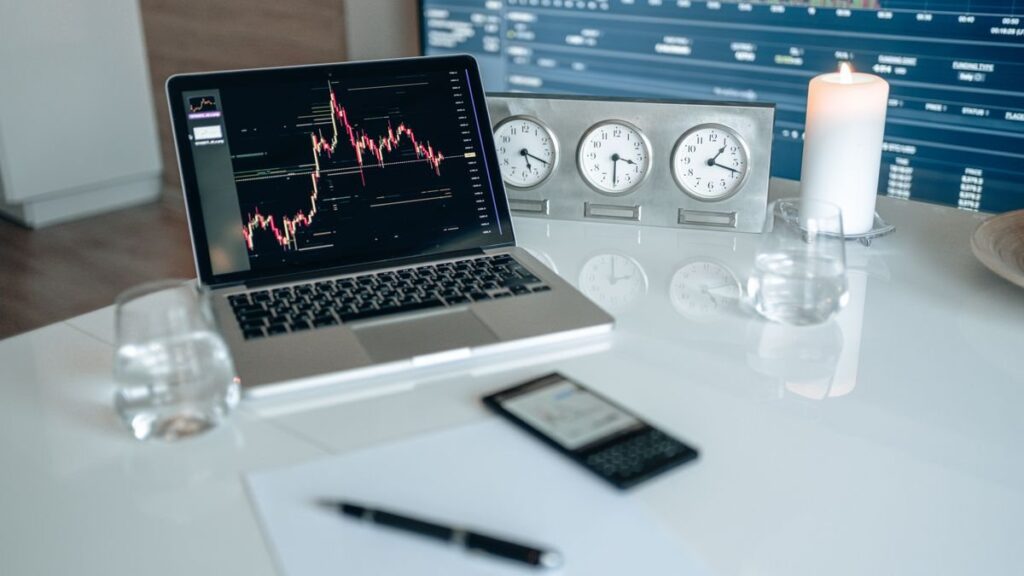 Laptop showing a price chart beside a row of clocks