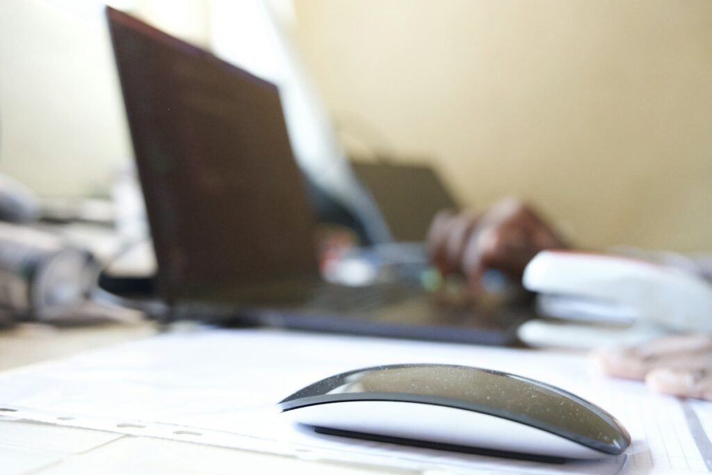 Computer mouse beside a laptop and papers on a desk