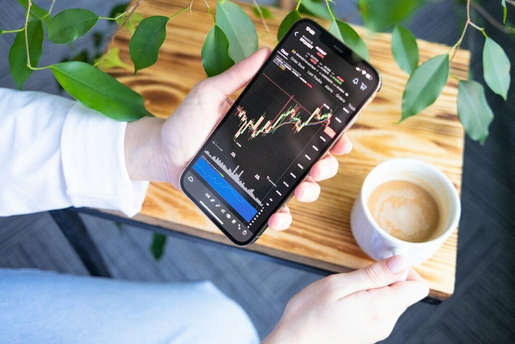 Hands holding a phone with a trading chart beside a cup of coffee