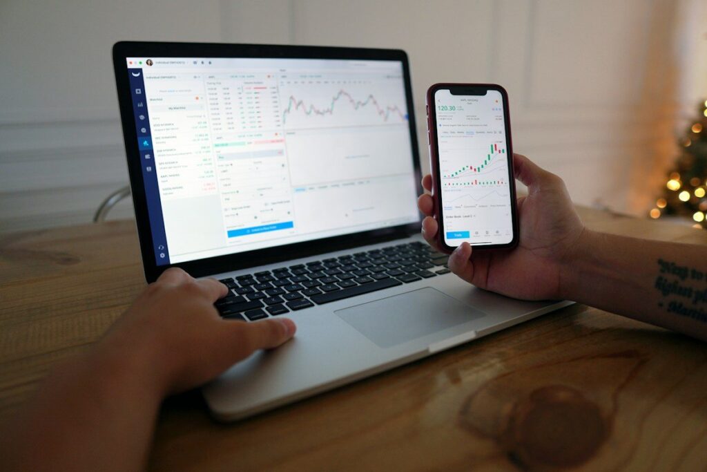 Hands on a laptop and a phone both showing price charts