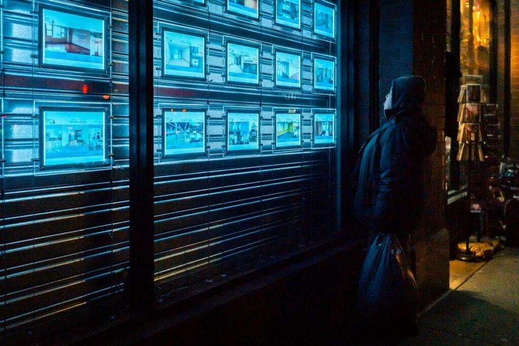 Person in a dark street looking at a lit display of screens