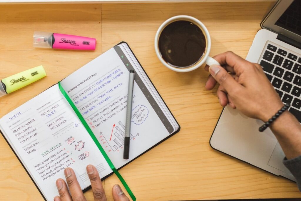 Trader writing notes in front of trading screens, listing the case against a trade before entry